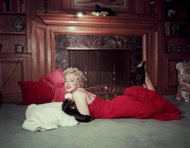 Portrait of Marilyn Monroe lying in front of a fireplace in a red dress