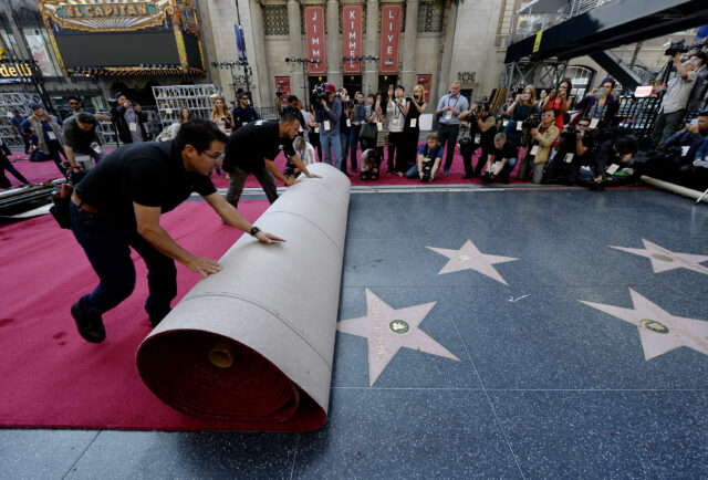 Photographers watching two men rolling a red carpet over the Hollywood Walk of Fame