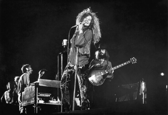 Janis Joplin performing on stage, a band behind her.