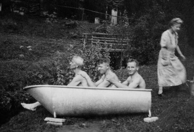 Three men sit is a bathtub, a woman walks by.