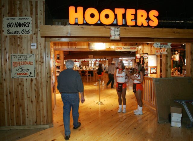 A man walking into a Hooters, two girls to greet him.