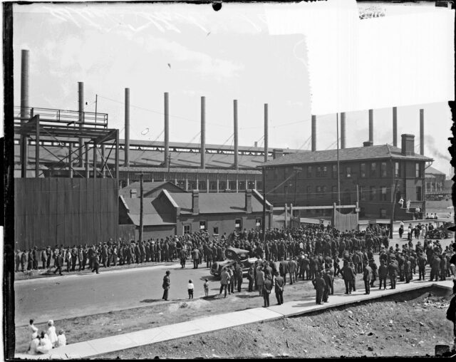 A group of people gathered out front of a steel mill.
