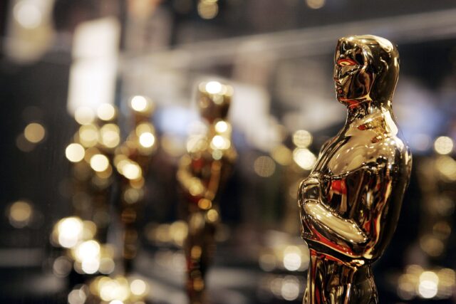 Several Oscar award statues lined up in a row, the ones in the background out of focus.