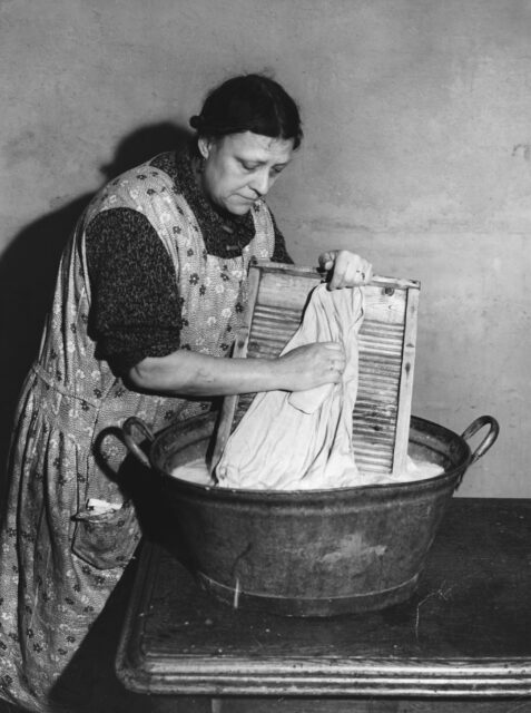 A woman washing linens over a washboard and bucket.
