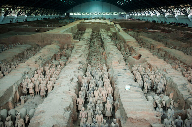 View looking down at rows of Terracotta soldiers covered by a dome, with some sections of destroyed stone.