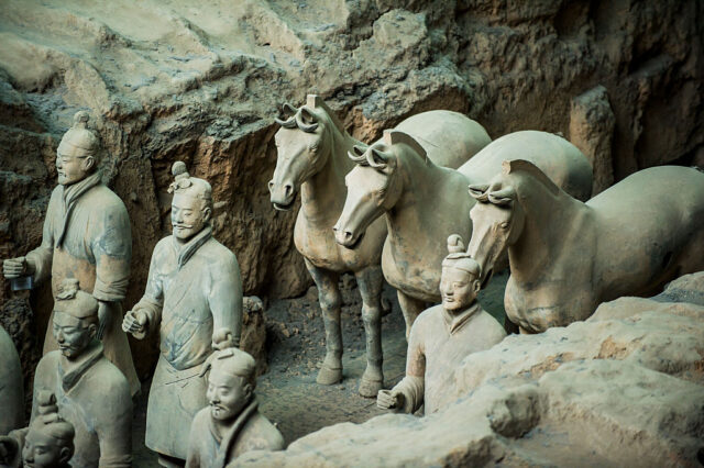 Three terracotta horses stand side by side behind a group of stone soldiers.