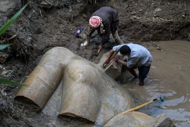 Two workers work on the upper torso section of the Psammetich I statue discovered in deep mud.