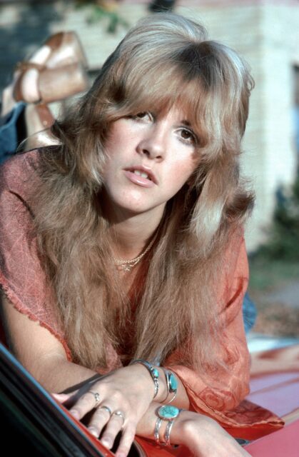 Headshot of a young Stevie Nicks laying on her stomach, leaning on her elbows