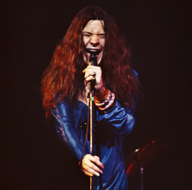 Jani Joplin singing hard into a microphone, her face wincing.