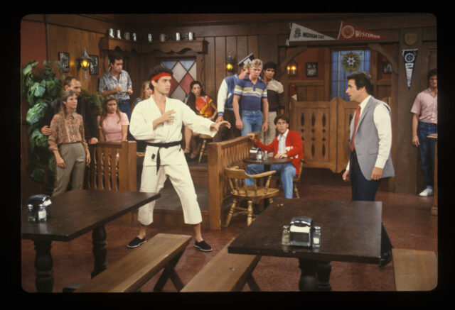 Tom Hanks in a karate uniform stands ready to fight Henry Winkler wearing a suit jacket with the sleeves ripped off in a scene from 'Happy Days.'