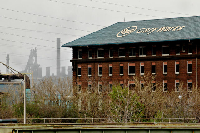 A building that reads "Gary Works" in the foreground, with the silhouette of a steel mill in the background.