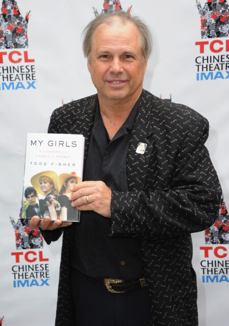 Todd Fisher holding up his memoir on a red carpet