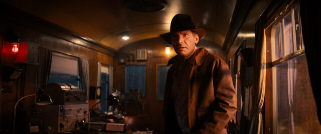 Harrison Ford as Indiana Jones, with VFX on his face to make him looking younger, standing in a train cart.