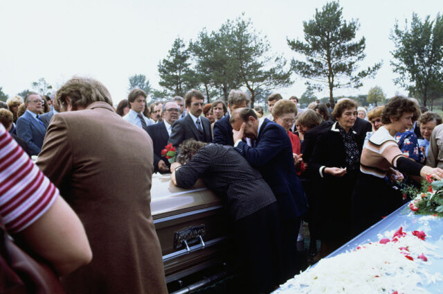 Funeral attendees crying over two coffins