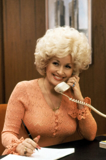 Dolly Parton smiling while holding a phone to her ear.