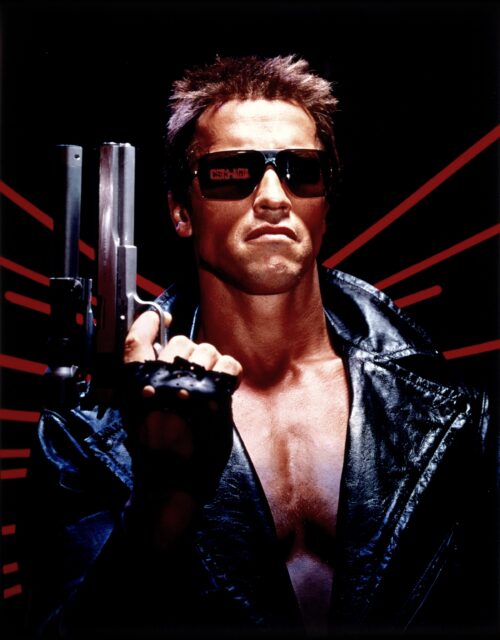 Arnold Schwarzenegger as the Terminator, in sunglasses and holding up a pistol.