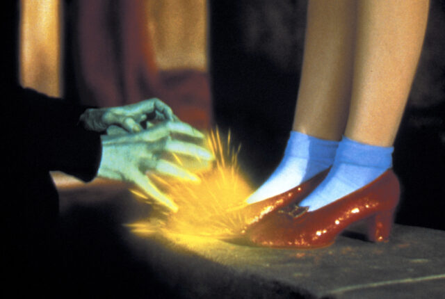Ruby slippers from "The Wizard of Oz", a witch's green hands emitting energy toward them.