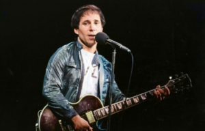 Paul Simon playing a guitar and singing into a microphone