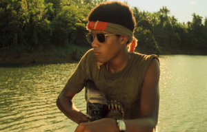 Young Laurence Fishburne in a t-shirt with rolled up sleeves, a bandana, and sunglasses.