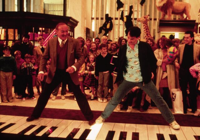 Tom Hanks and Robert Loggia playing a floor piano, a group gathered behind them.