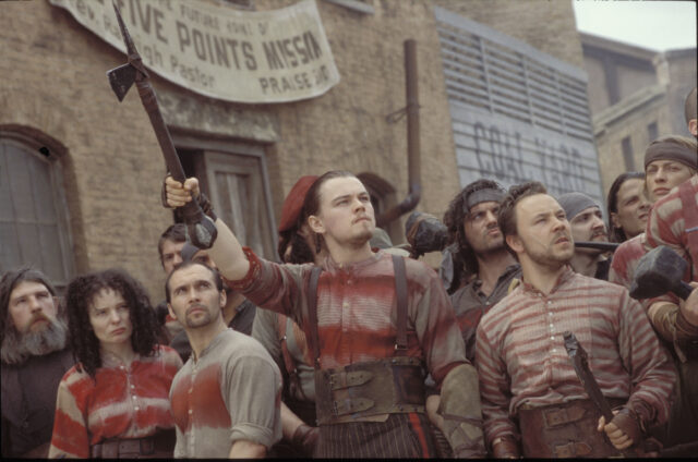 Leonardo DiCaprio and others walking in a group, DiCaprio lifting a rifle in the air.