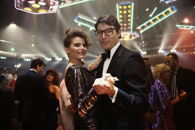 Christopher Reeve in a black suit, bow tie, and glasses, dancing with Mariel Hemingway who wears a sparkling dress. 