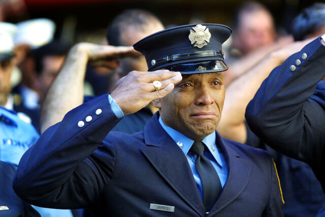 Firefighter Tony James wears a formal uniform as he stands at attention with tears running down his face.