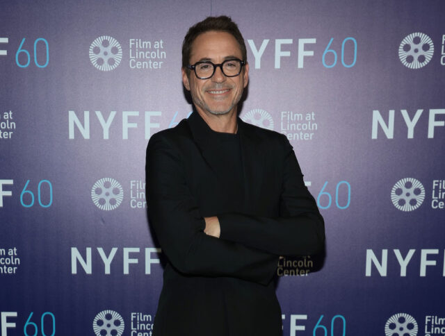 Robert Downey Jr. in a black suit and shirt, posing with his arms crossed. 