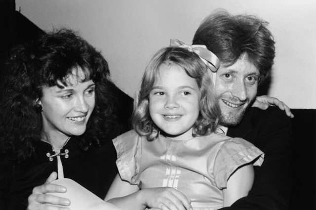 A young Drew Barrymore sitting with her mother and uncle.