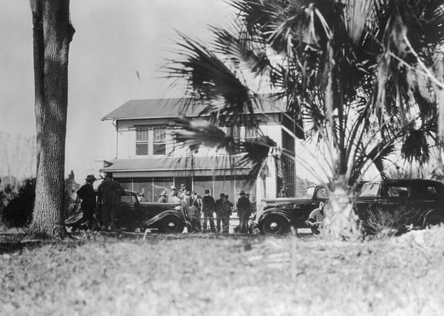 Distanced view of a house surrounded by police and palm trees.