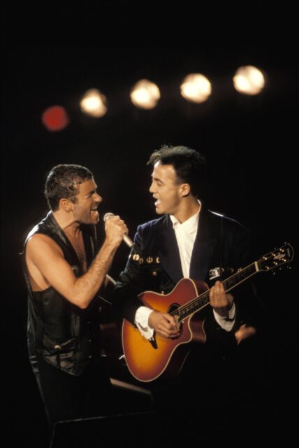 George Michael and Andrew Ridgeley singing with one another, the latter holding a guitar