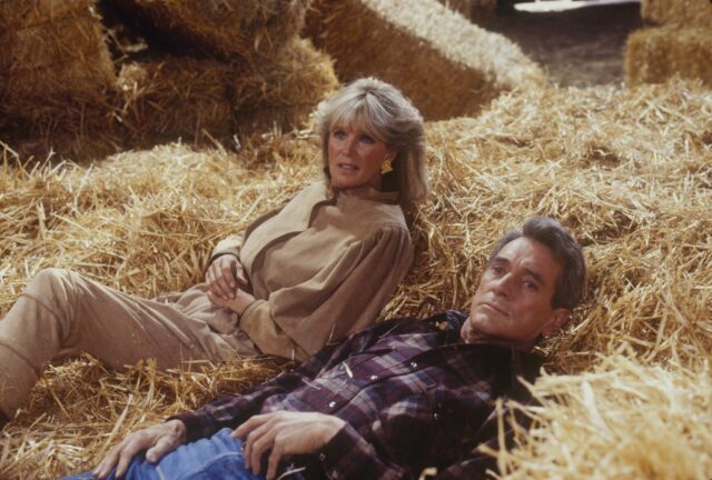 Linda Evans and Rock Hudson lying beside each other is a hay bale. 
