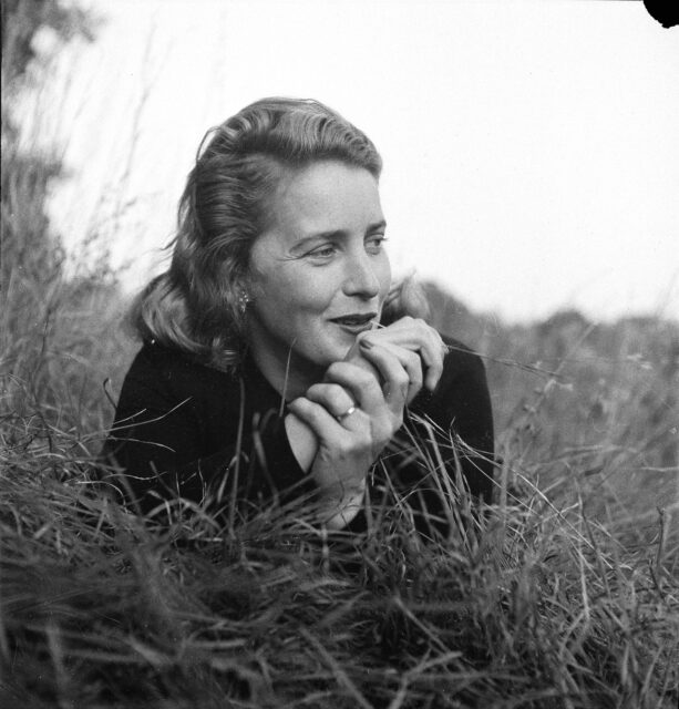 Margaret Wise Brown lying in the grass with a blade of grass between her teeth.