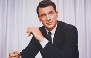 Rock Hudson seated, elbows resting on his knees.