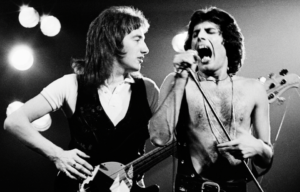John Deacon and Freddie Mercury of Queen performing on stage.