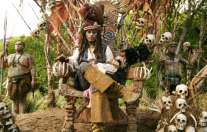 Johnny Depp as Jack Sparrow sitting in a chair surrounded by human skulls with his legs crossed.