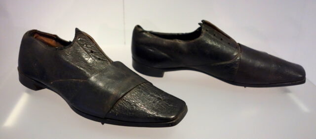 A pair of leather dress shoes with spikes underneath on display.