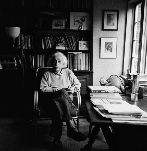Albert Einstein sits at a desk in his study