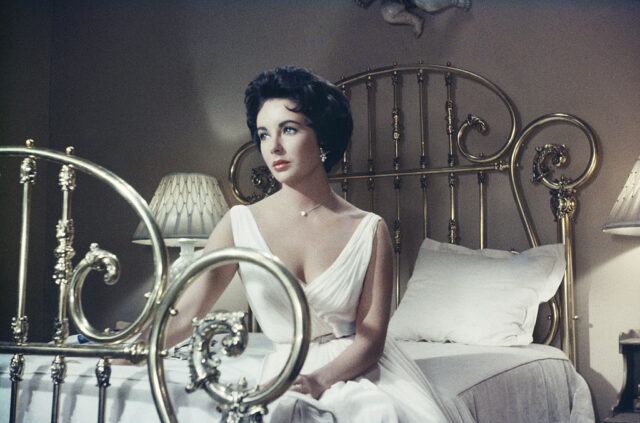Elizabeth Taylor sits on a bed while filming 'Cat On A Hot Tin Roof'