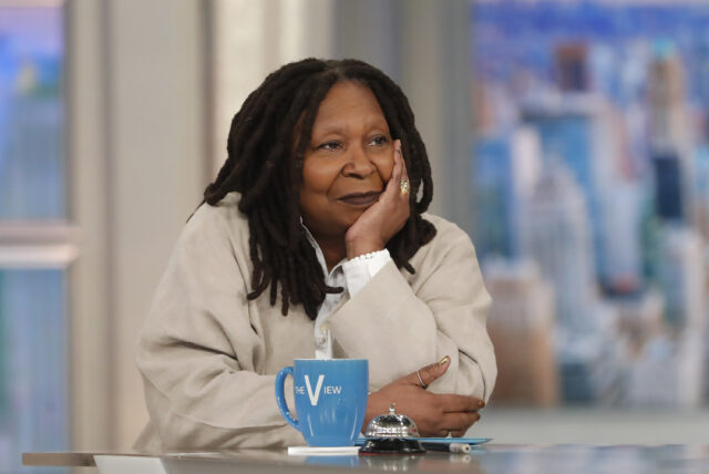Whoopi Goldberg resting her head in her hand at a table.