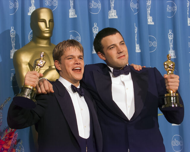 Matt Damon and Ben Affleck with their arms around one another holding their Oscar awards.