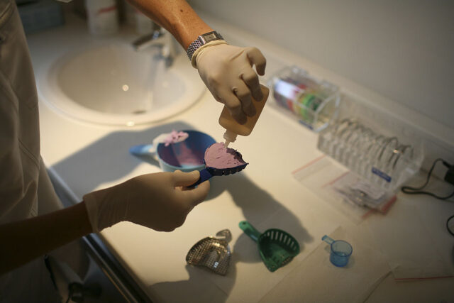 View of person's hands preparing dental mold paste in a container over a sink.