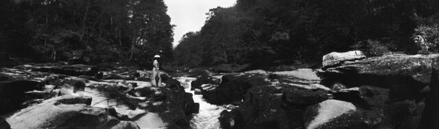 Woman in a victorian dress stands on the rocky banks of the Bolton Strid.