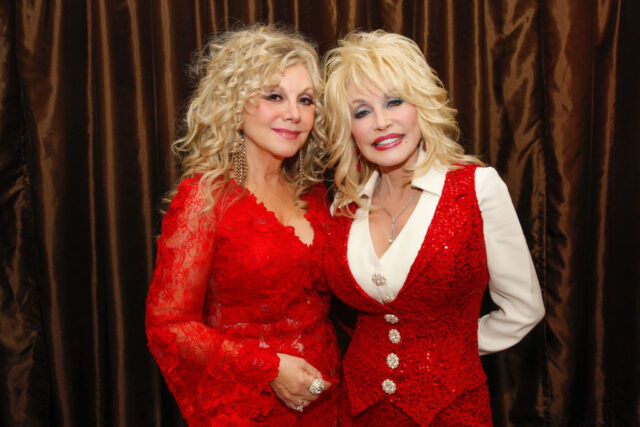Stella Parton in a red lace dress, and Dolly Parton in a white shirt with a red sequin vest.