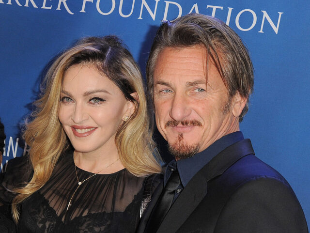 Sean Penn and Madonna pose in black clothing in front of a blue backdrop on the red carpet.