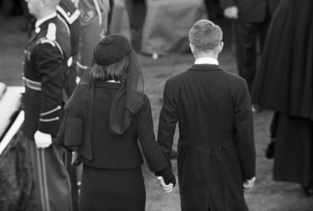 Jackie Kennedy and Robert F. Kennedy holding hands and walking away at JFK's funeral.