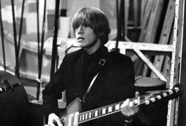 Brian Jones with holding a guitar strapped around him.