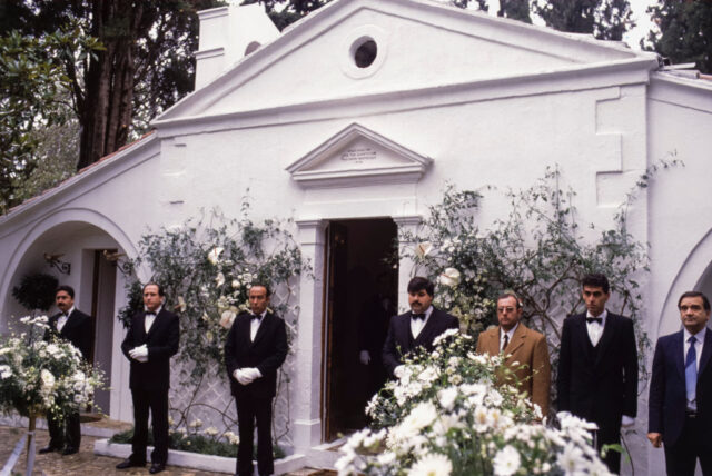 Men standing in suits along the exterior of a chapel