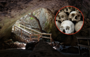 A photo from the inside of a cave looking at its opening, a collection of skulls on top.