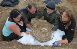 Four people lift up a the Euston hoard from a hole in the ground.